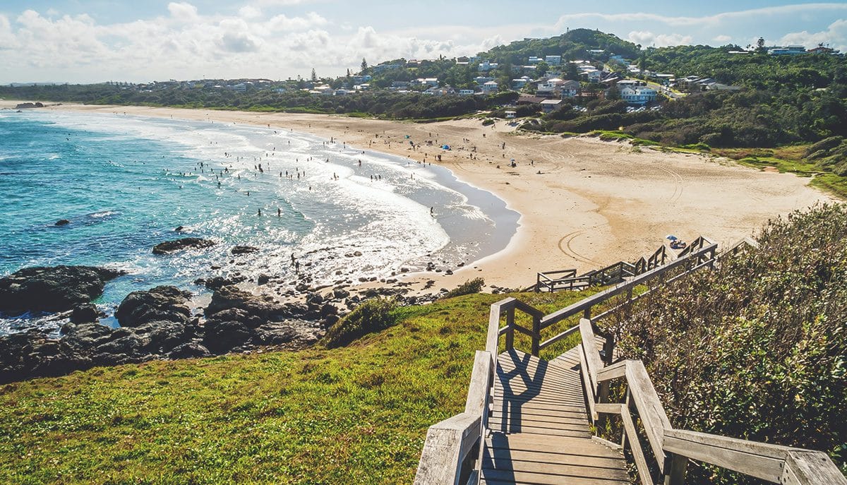 Wooden stairs lead to a populated beach and ocean.