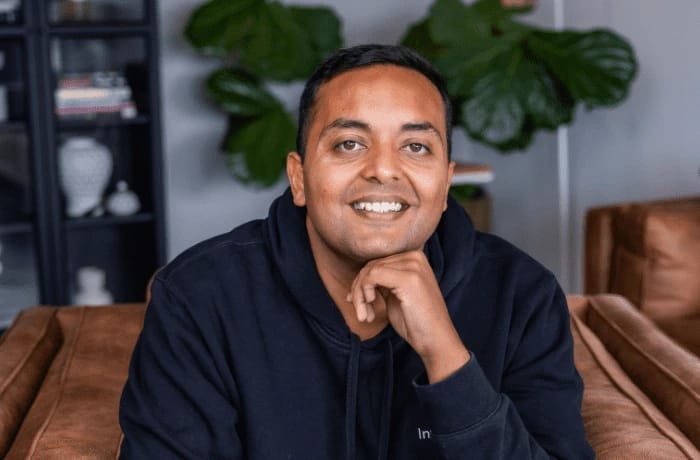 Man in dark hoodie resting chin on hand, smiling.