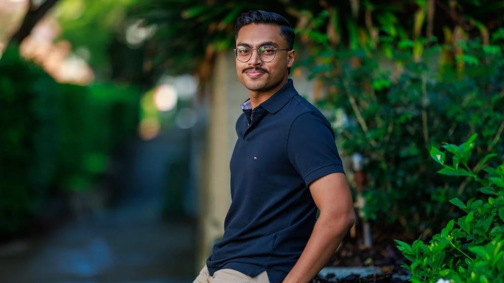 Man in a navy polo and glasses smiling outdoors.