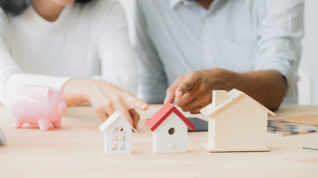 Miniature houses, piggy bank, and hands pointing.