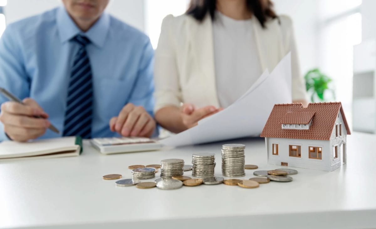 Model house and coins on a desk with people discussing documents.