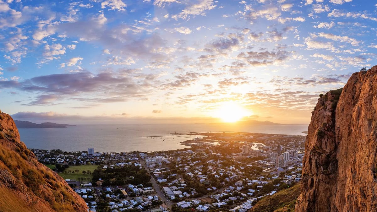 Coastal city at sunset viewed from rocky outcrop.