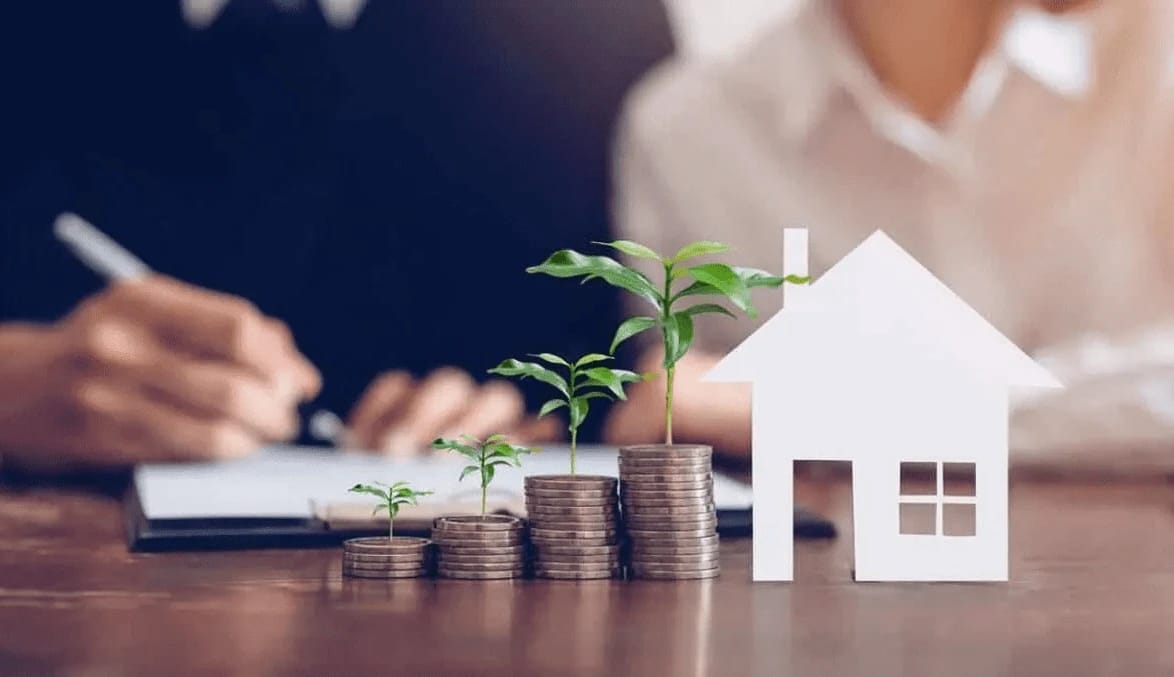 Coins stacked like stairs with plants, house cutout, person writing