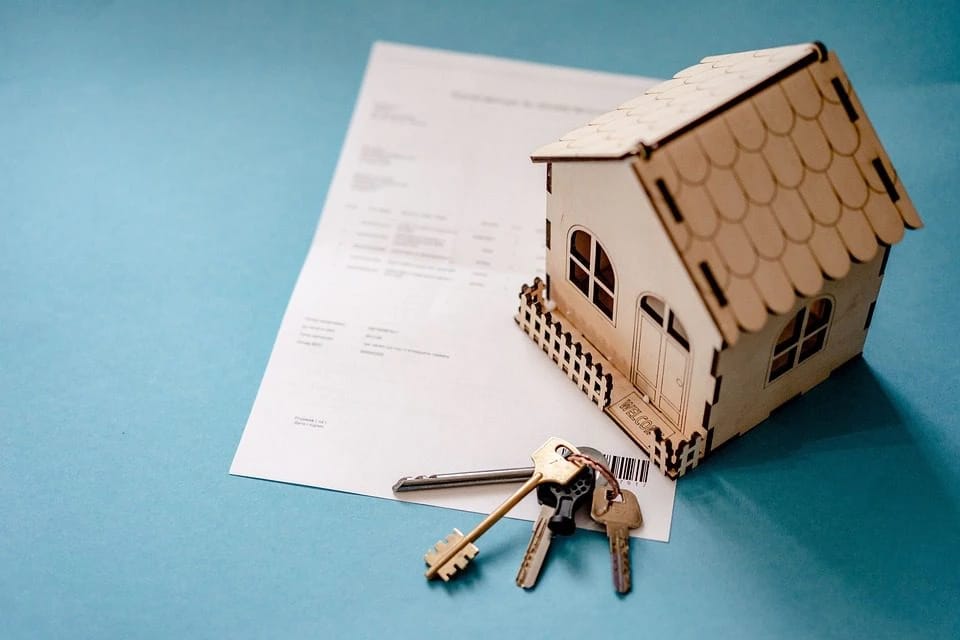 Model house, keys, and document on blue surface.