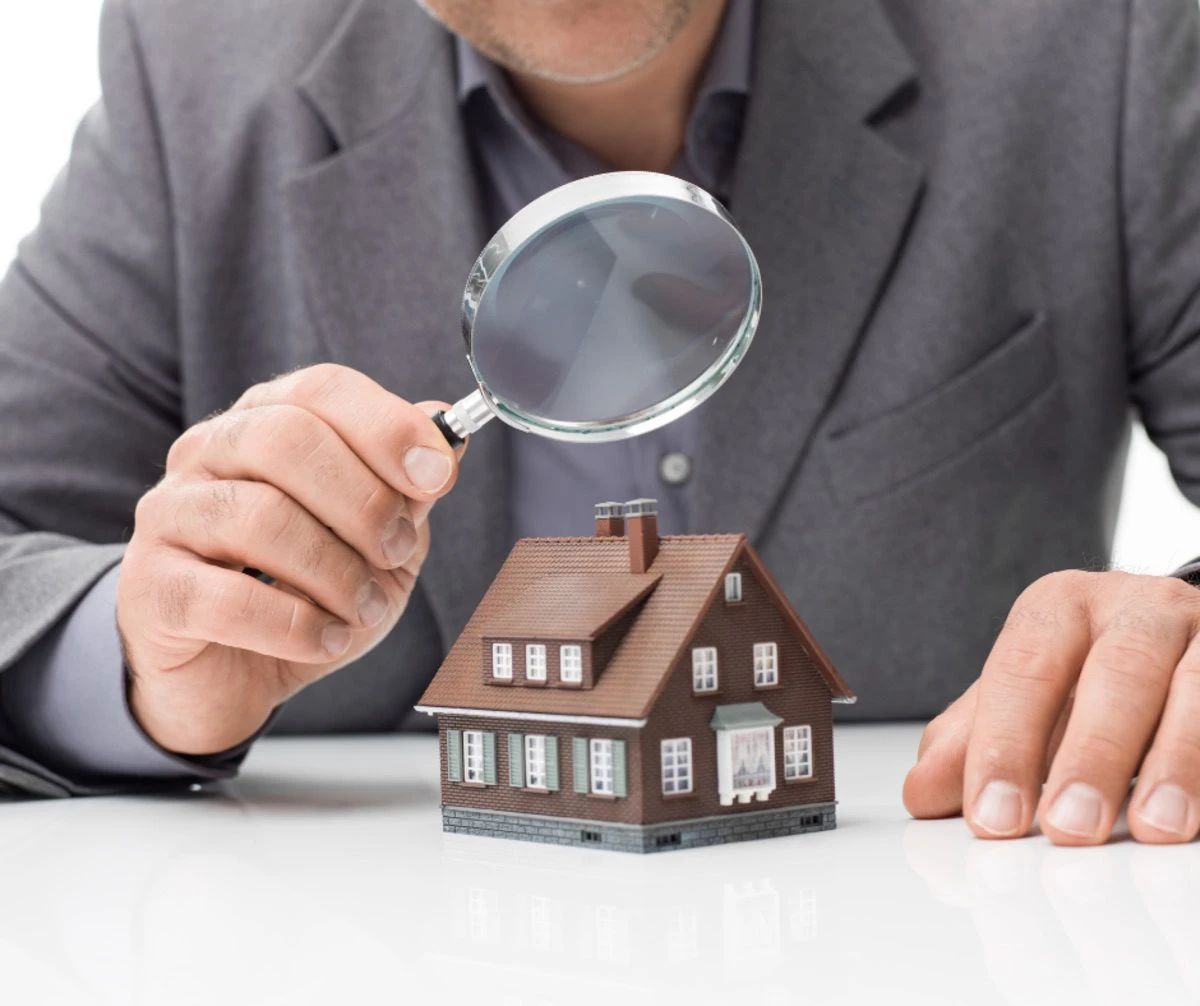 Man examines miniature house with magnifying glass