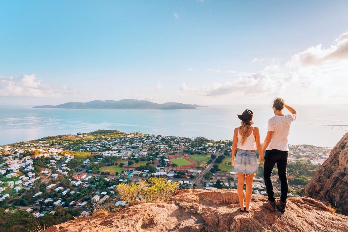 Couple holding hands on a cliff overlooking a town and ocean.