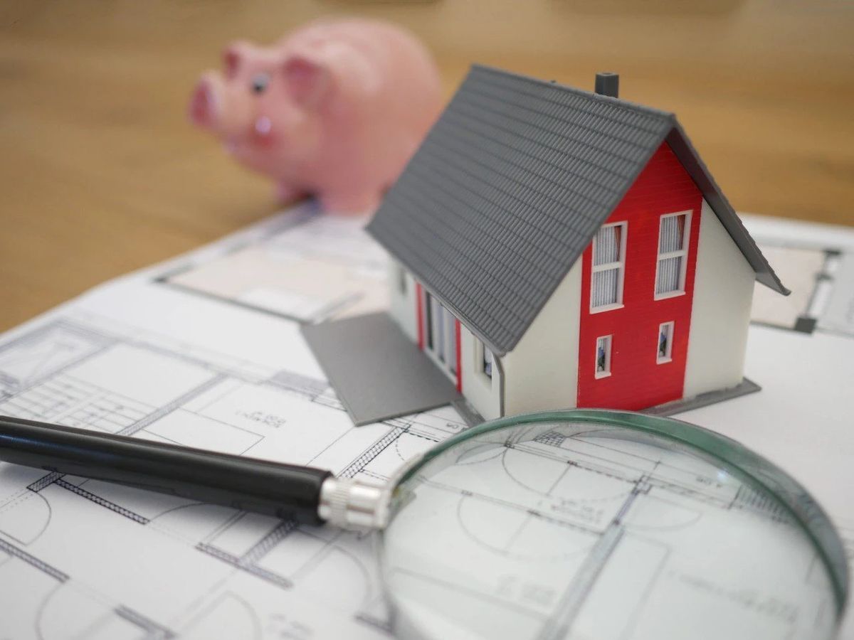 House model, piggy bank, blueprints, and magnifying glass.