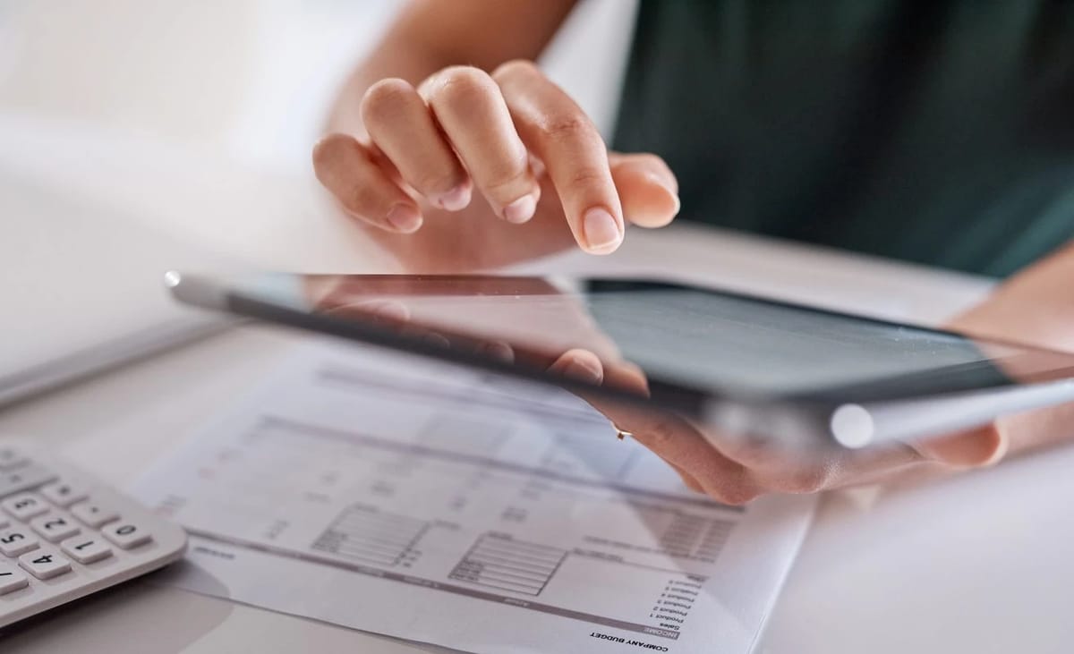Fingers interacting with a tablet over a budget sheet.