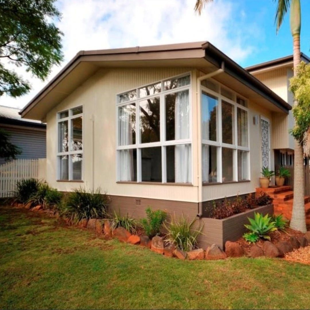 Cream house with white-framed bay windows and lawn.