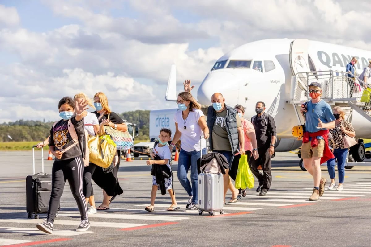 Passengers deplaning with luggage in front of a Qantas airplane.