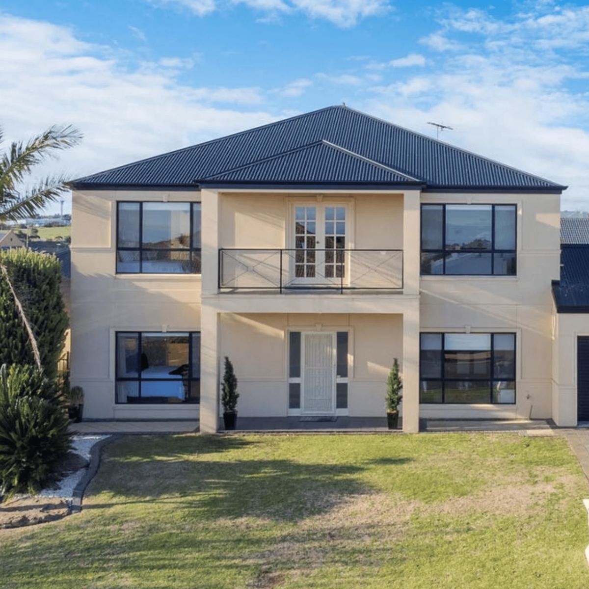 Two-story beige house with a dark metal roof.