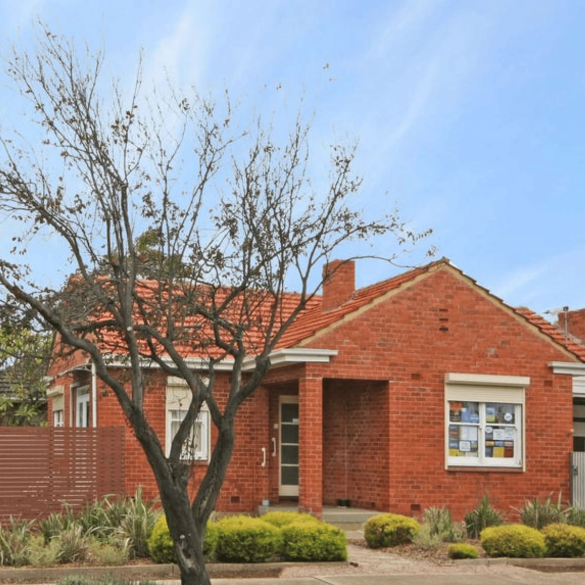 Red brick house with bare tree and blue sky.