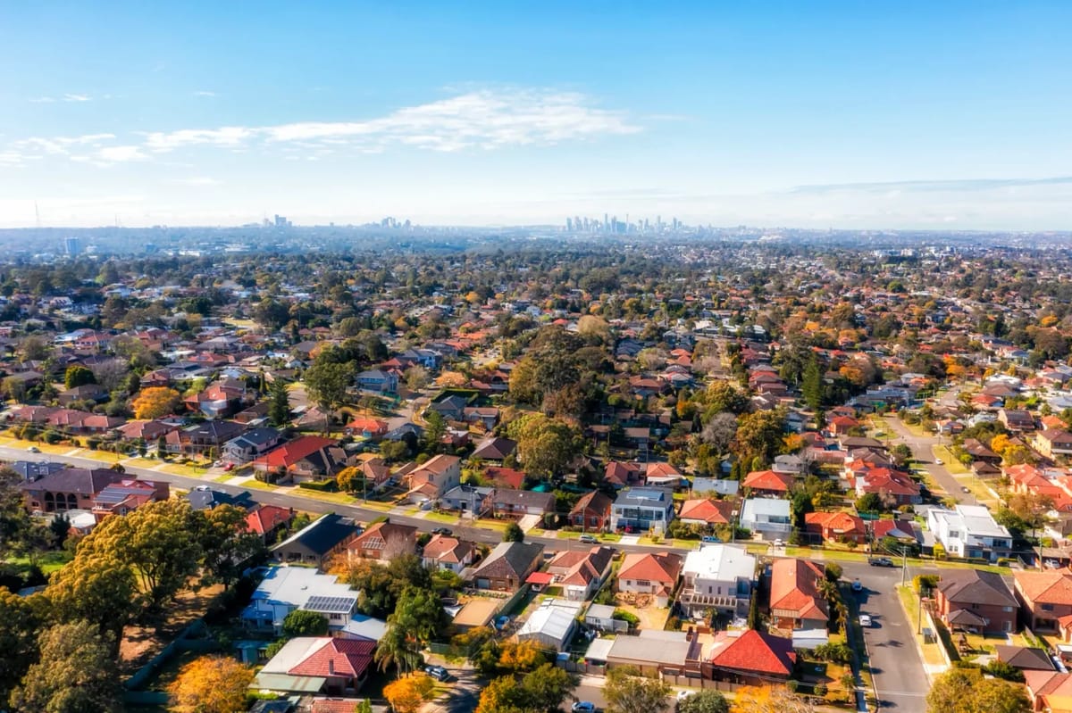 Suburban rooftops and distant city skyline under blue sky.
