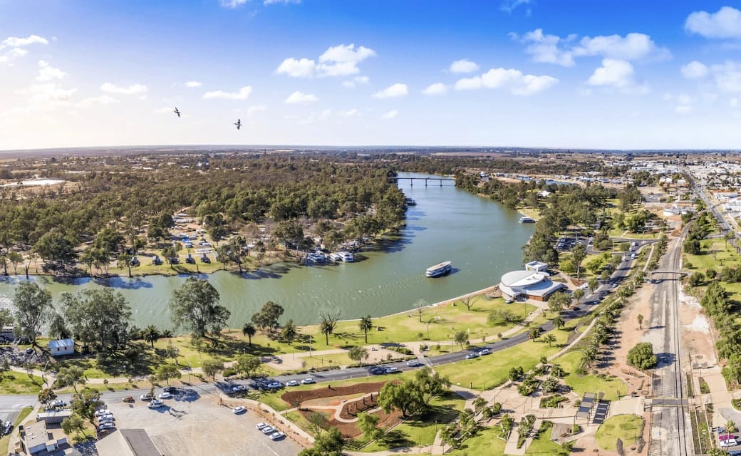 Riverfront with buildings, park, and birds in sky