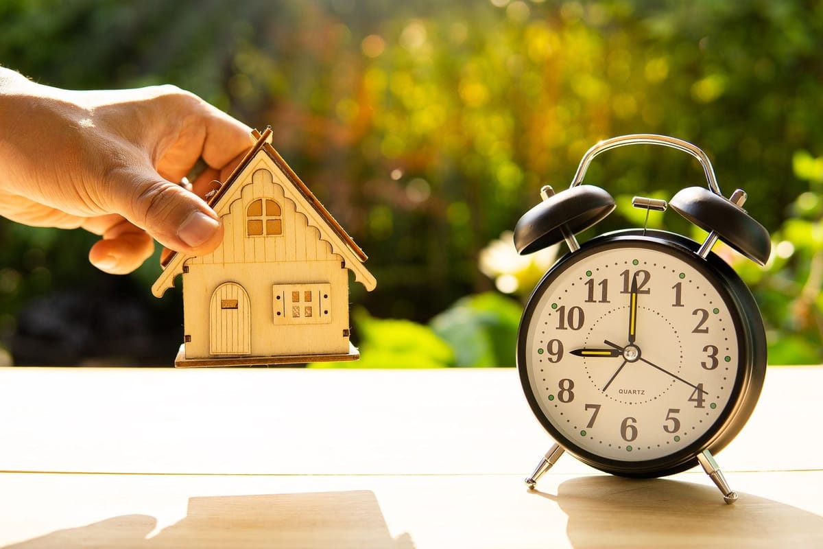Hand holding model house next to alarm clock