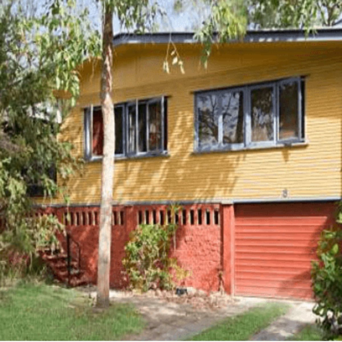 Raised yellow weatherboard investment home with a red garage door in Townsville, Queensland