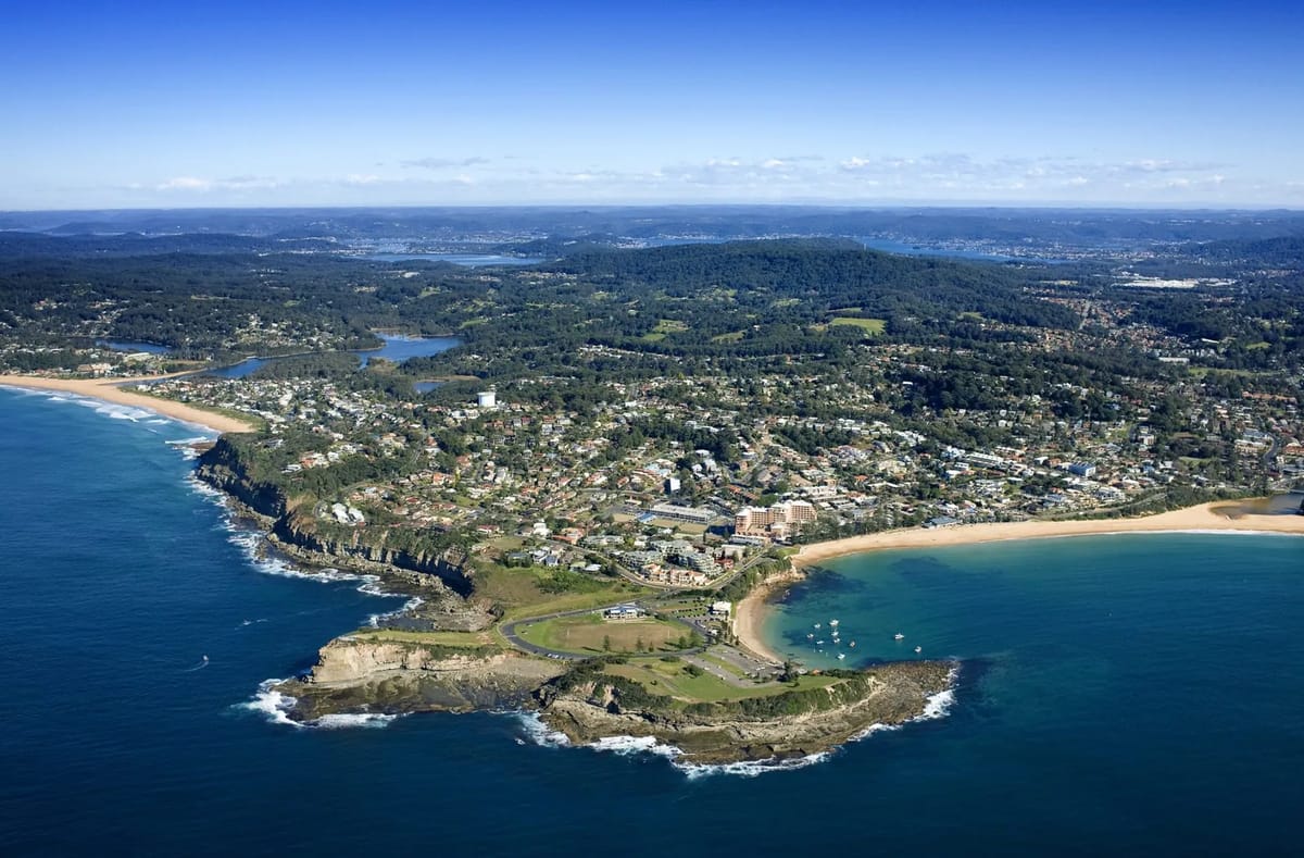 Coastal town with beaches and hilly, tree-covered landscape.