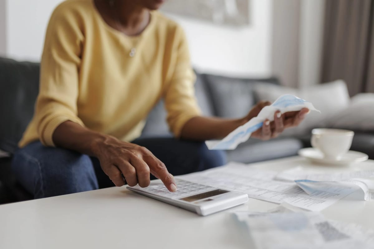 Person using a calculator with bills and a cup of coffee.