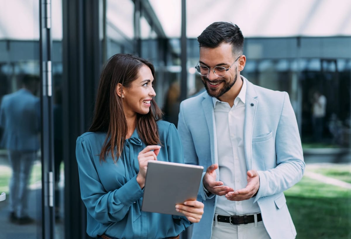 Colleagues discussing a tablet outside an office building.