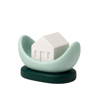 Ceramic illustration of a small white house held in a cupped green base.