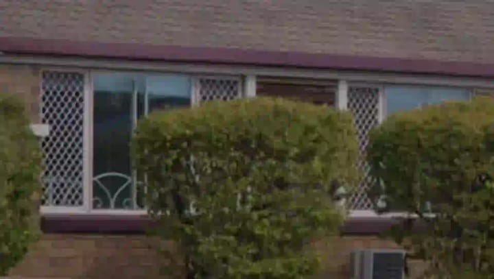 The right-hand side of a single-storey brick house in Annandale, with a tiled roof, windows, an air conditioner and shrubs